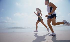 Two people running on the beach near water.